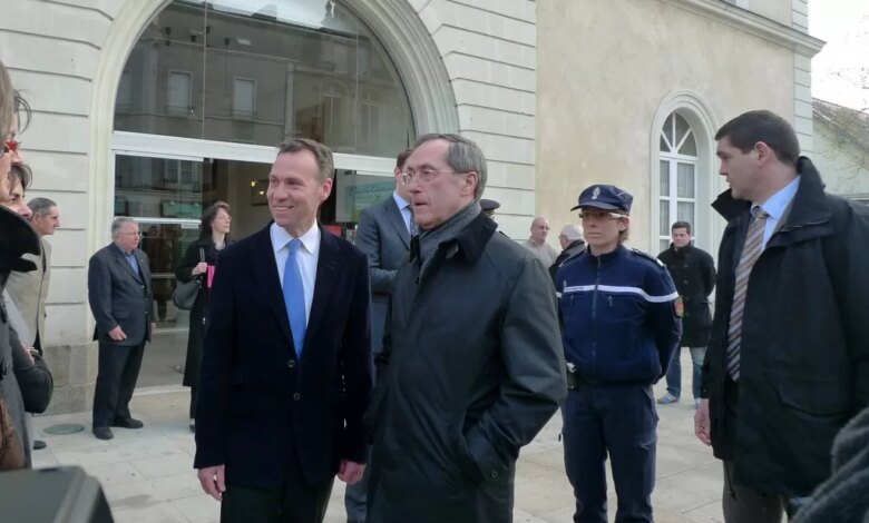 Un groupe d'hommes en tenue de soirée se tient devant un bâtiment à Nantes. Au premier plan, deux hommes, l'un en costume, l'autre en manteau, sont en pleine conversation. Un policier et d'autres personnes s'attardent à proximité, leur présence ajoutant à l'atmosphère d'anticipation typique des rassemblements en Loire-Atlantique.