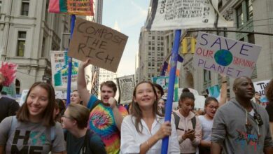 Un groupe de personnes de tous horizons défile dans une ville, brandissant des banderoles pour réclamer des mesures pour le climat. Des pancartes telles que Compost the Rich et Save Our Burning Planet se démarquent, les participants semblant engagés et déterminés. De hauts immeubles bordent la rue tandis que les médias locaux comme Actu44.fr couvrent cette manifestation passionnée.