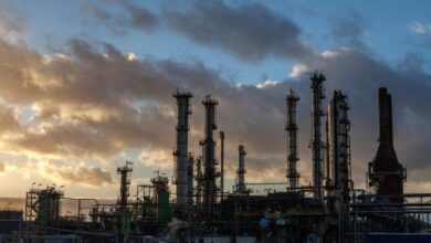 L'usine industrielle de Châteaubriant se dresse avec ses hautes cheminées se détachant sur un ciel spectaculaire au coucher du soleil. Des nuages sombres planent au-dessus, tandis que la chaude lueur du soleil couchant met en valeur les structures en acier et les canalisations complexes de cette usine de Loire-Atlantique.