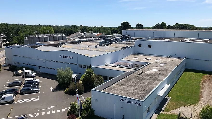 Vue aérienne d&#039;un complexe industriel à Châteaubriant avec le logo Tetra Pak sur plusieurs grands bâtiments blancs. Entourés par la verdure luxuriante de la Loire-Atlantique, des voitures stationnées et des équipements extérieurs sont visibles aux alentours, mettant en valeur l&#039;harmonie entre l&#039;industrie et la nature.