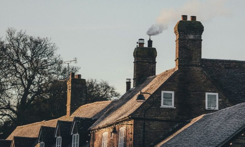 Une rangée de maisons en briques avec cheminées, dont l'une dégage de la fumée, évoque une matinée sereine à Châteaubriant. Les toits sont légèrement recouverts de givre tandis que les arbres nus se dressent sur un ciel clair de Loire-Atlantique, soulignant le charme tranquille de la région.