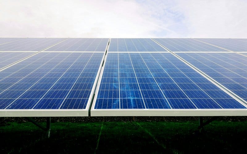 Un grand ensemble de panneaux solaires se dresse devant un ciel nuageux à Châteaubriant, captant la lumière du soleil pour produire de l&#039;énergie. Les panneaux sont installés sur un terrain herbeux en Loire-Atlantique, mettant l&#039;accent sur les énergies renouvelables et la durabilité.