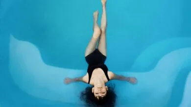 Une personne en maillot de bain noir flotte sur le dos dans une piscine d'un bleu limpide près de Châteaubriant, les yeux fermés et les bras écartés. L'eau semble calme, créant une atmosphère sereine et paisible typique de la région pittoresque de la Loire-Atlantique.