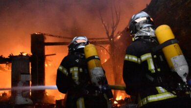 Deux pompiers en tenue complète, casque et bouteille d'oxygène compris, luttent contre un important incendie qui ravage une structure à Châteaubriant. Les flammes et la fumée envahissent la scène tandis qu'ils pulvérisent de l'eau avec un tuyau, mis en valeur par la lueur orange intense du brasier, attirant l'attention à Nantes et sur Actu44.fr.